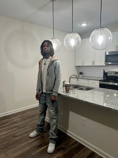 a man standing in front of a kitchen counter with three lights hanging from the ceiling