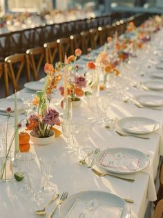 a long table is set with white plates and place settings for an elegant dinner party