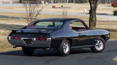 a black muscle car parked on the side of a road in front of trees and grass