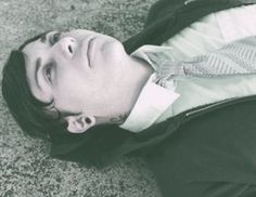 a young man wearing a suit and tie laying on the ground with his head down