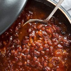 a pot filled with chili and beans on top of a table next to a spoon