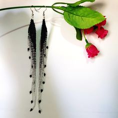 two black and white beaded necklaces hanging from a green leaf next to red flowers