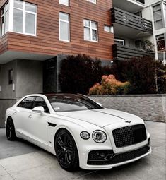 a white car is parked in front of a brown building with balconies on it