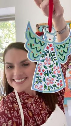 a woman holding up a paper angel ornament in front of her face and smiling at the camera