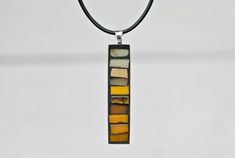 a multicolored glass pendant hangs from a leather cord on a white wall background