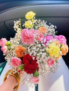 a bouquet of flowers sitting on top of a white cloth covered car seat in front of a person's hand