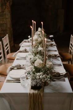 a long table is set with white flowers and candles for an elegant dinner or reception