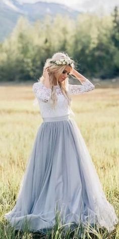 a woman standing in a field wearing a dress with sleeves and a flower crown on her head