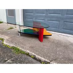 a glass table sitting on the sidewalk in front of a garage door with an artistic design