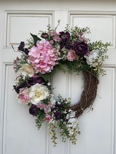 a wreath is hanging on the front door with purple and white flowers around it,