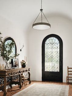 a room with a table, mirror and chair in front of a door that has an arched window