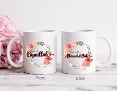 two coffee mugs sitting next to each other on a table with flowers in the background