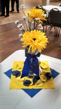 a vase filled with yellow and white flowers on top of a blue table cloth covered table