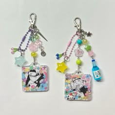 two keychains with charms attached to them on a white surface, one has a cartoon character and the other has a bottle