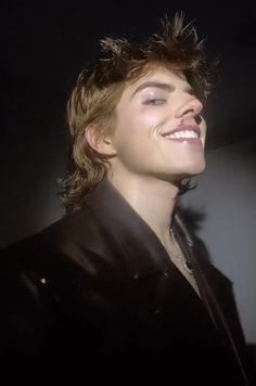 a young man smiling and wearing a leather jacket