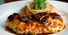 a white plate topped with meat covered in sauce and mushrooms next to pasta on a wooden table