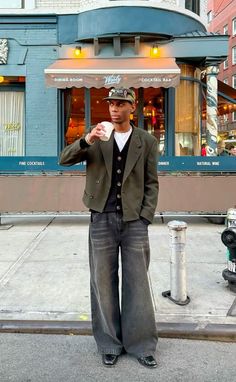 a man standing in front of a building with his hand up to his mouth while holding a coffee cup