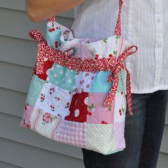 a woman holding a colorful patchwork purse with red ribbon around the strap and handles