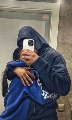 a woman taking a selfie in front of a mirror with her cell phone while wearing a hoodie