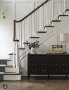 a black dresser sitting in front of a stair case next to a white wall and wooden floor