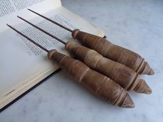 three old wooden spoons sitting next to an open book on a marble counter top