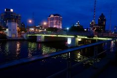 a bridge that is over some water with buildings in the backgroung and lights on