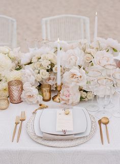 the table is set with white flowers and gold place settings for an elegant wedding reception