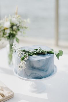 a blue marbled cake with flowers and greenery on the top sits on a white table