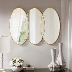 three round mirrors on the wall above a table with vases and flowers in front of it