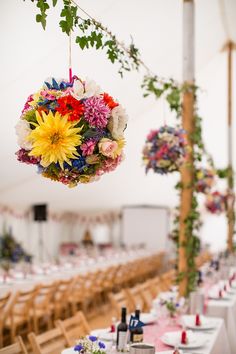 an arrangement of flowers hanging from the ceiling in a tent with tables and chairs set up