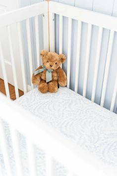 a brown teddy bear sitting on top of a white crib