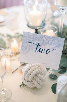 a place card with the word two is placed on top of a table surrounded by candles and greenery