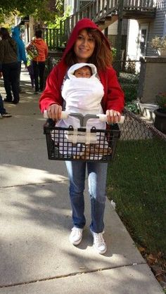 a woman is holding a baby in a stroller on the sidewalk while wearing a costume