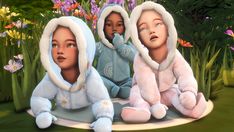 three children dressed in winter clothing sitting on the ground next to flowers and grass, with one looking up at the camera