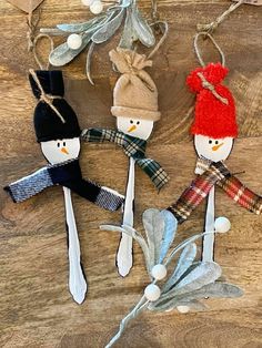 three snowman ornaments are hanging on a wooden table