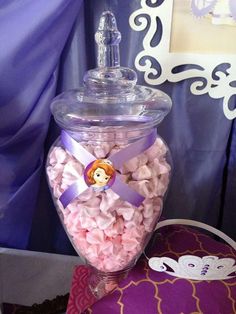 a glass jar filled with pink and purple candies on top of a table next to a pillow