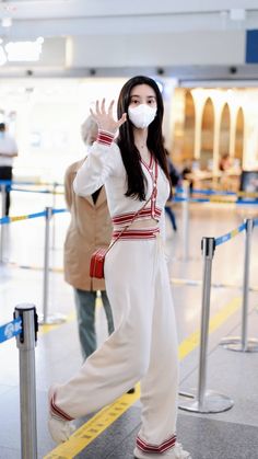 a woman wearing a mask while standing next to a metal pole with her hand up in the air