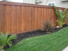 a wooden fence in front of a house with green grass and plants next to it