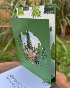 a close up of a greeting card on a wooden table with plants and trees in the background