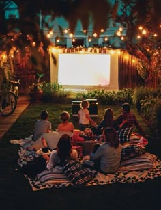 a group of people sitting on top of a blanket in front of a movie screen