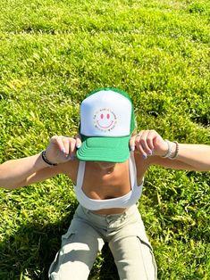 a woman laying in the grass wearing a green and white hat with a smiley face on it