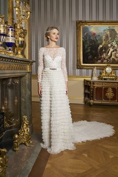 a woman standing in front of a painting wearing a long white dress with ruffles