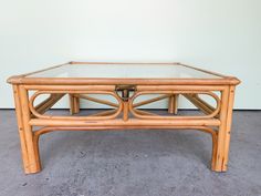 a coffee table made out of bamboo with glass top on concrete floor next to white wall