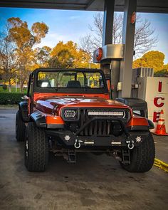 an orange jeep is parked at a gas station