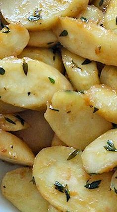 a white bowl filled with potatoes covered in seasoning and sprinkled with herbs