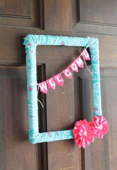 a welcome sign hanging on the front door with pink and blue paper flowers attached to it