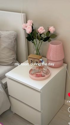 a white nightstand with pink flowers on it next to a night stand and bedding