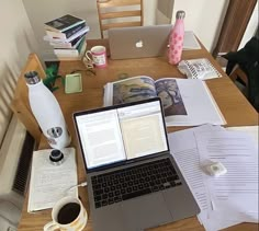 an open laptop computer sitting on top of a wooden table next to books and papers