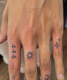 a woman's hand with tattoos on it and two fingers that have arrows, stars, and the moon