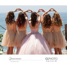 four bridesmaids in pink dresses are making a heart shape with their hands at the beach